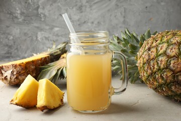 Tasty pineapple juice in mason jar and fresh fruits on grey textured table, closeup