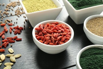 Different healthy superfoods in bowls on black wooden table, closeup