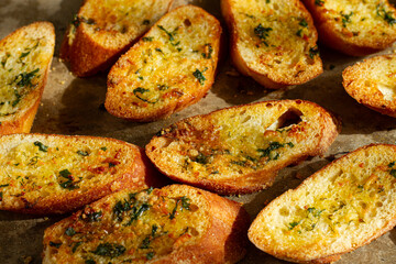 baguette toasts, baked in the oven, with garlic butter and herbs, homemade, on a platter, top view,