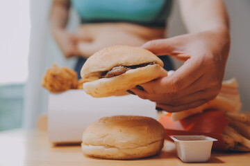 To eat or not. Cheerless plump woman looking at the burger while thinking to eat it or not