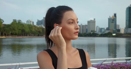 Woman inserts earphones prepares for leisurely walk with music in ears enjoying sounds amidst urban bustle. Musical compositions in earphones special mood for walk. Woman finds tranquility earphones.