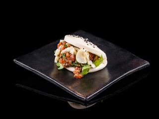 Gourmet Asian bao bun with fresh ingredients on black plate