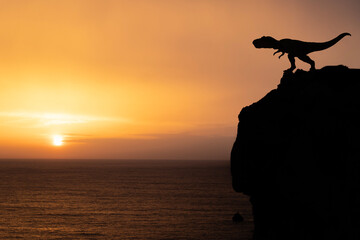 Silhouette of tyrannosaurus on sea promontory at sunset.