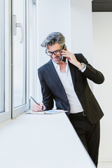 An elegant executive talking on his mobile phone, next to a window, symbolising connected businesses