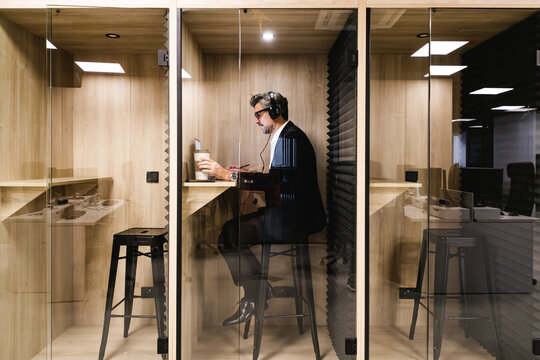 An executive engrossed in work uses headphones in a soundproof booth, ensuring privacy and concentration in a modern office