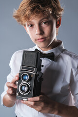 Fototapeta premium Preteen boy in white shirt and bow tie holding vintage photo camera