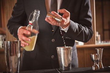 Barkeeper pouring alcohol in cocktail shaker from jigger