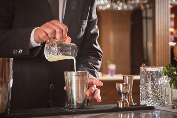 Bartender pouring cocktail from flask in shaker in nightclub
