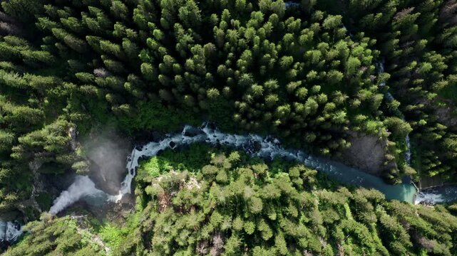 Cascate del rutor waterfall winding through dense forest greenery in summer, aerial view