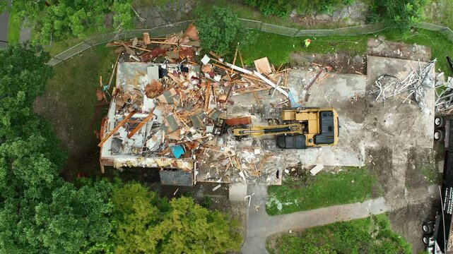 Excavator demolishing house. Ground level demolition with debris falling. Aerial of condemned home being torn down. Excavator at work. Aerial top down.
