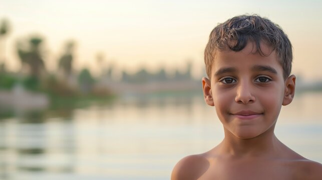 A young boy smiles warmly at the camera with a water body and a serene sunset backdrop, capturing innocence, joy, and natural beauty.