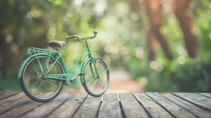 Fototapeta premium A vintage mint-green bicycle stands alone on a wooden platform, surrounded by lush, blurred greenery under the warm sunlight.