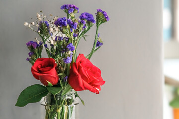 A bouquet of fresh roses with baby breath in a glass water jar on white background.