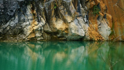 An image of a rocky cliff face reflected in the calm, emerald-green waters of a lake.