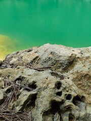 An image of a rocky shoreline with jagged stone formations along the edge of a calm, emerald-green lake.