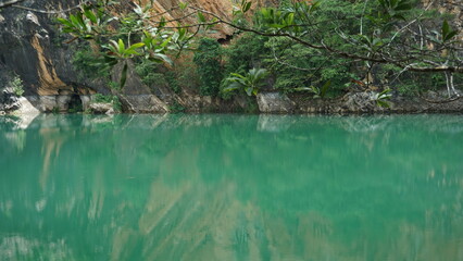 An image of a peaceful emerald-green lake with a backdrop of rocky cliffs and lush greenery.