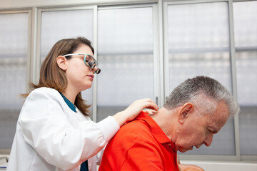 Fototapeta premium Dermatologist making a routine checkup on a senior male patient using a binocular loupe.