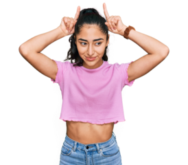 Hispanic teenager girl with dental braces wearing casual clothes doing funny gesture with finger over head as bull horns