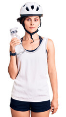 Beautiful young woman with short hair wearing bike helmet and holding water bottle thinking attitude and sober expression looking self confident