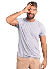 Young hispanic man wearing casual clothes doing ok gesture with hand smiling, eye looking through fingers with happy face.