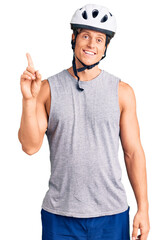 Young handsome man wearing bike helmet showing and pointing up with finger number one while smiling confident and happy.