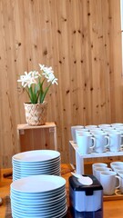 Warm wooden tables adorned with vibrant flower in eco-friendly cafe.Clean plates and cups are thoughtfully arranged, inviting guests to enjoy nature-inspired dining experience Eco-friendly ambiance 