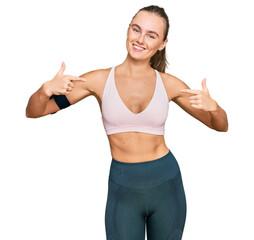 Beautiful young blonde woman wearing sportswear and arm band looking confident with smile on face, pointing oneself with fingers proud and happy.