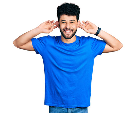 Young arab man with beard wearing casual blue t shirt smiling pulling ears with fingers, funny gesture. audition problem