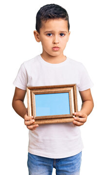 Little cute boy kid holding empty frame thinking attitude and sober expression looking self confident