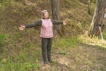 A person stands with arms open wide, embracing nature in a vibrant green forest under bright daylight.
