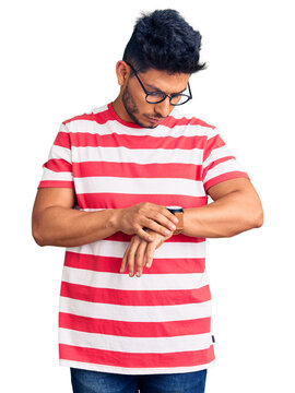 Handsome latin american young man wearing casual clothes and glasses checking the time on wrist watch, relaxed and confident