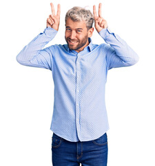 Fototapeta premium Young handsome blond man wearing elegant shirt posing funny and crazy with fingers on head as bunny ears, smiling cheerful