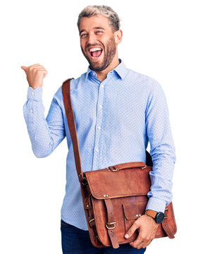Young handsome blond man wearing elegant shirt holding briefcase pointing thumb up to the side smiling happy with open mouth