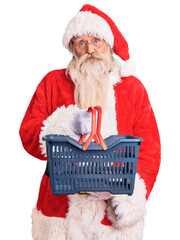 Old senior man with grey hair and long beard wearing santa claus costume holding shopping basket...