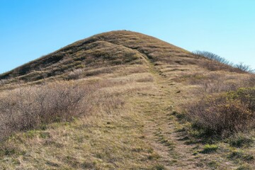 Fototapeta premium A solitary path leading up a grassy hill under a clear blue sky, suggesting a trek or exploration theme.