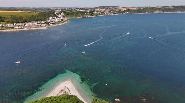 Looe Island with boats in calm blue waters and green cliffs with shoreline in the background