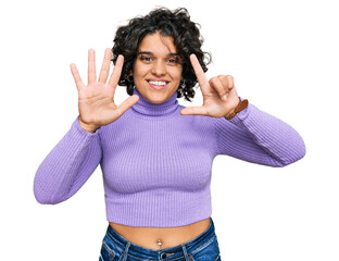 Young hispanic woman with curly hair wearing casual clothes showing and pointing up with fingers number seven while smiling confident and happy.