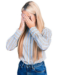 Beautiful blonde woman wearing casual striped shirt with sad expression covering face with hands while crying. depression concept.