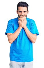 Young handsome man with beard wearing casual t-shirt laughing and embarrassed giggle covering mouth...