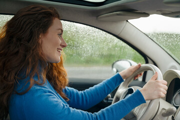 Naklejka premium Woman Driving Car on Rainy Day While Smiling in Suburban Area