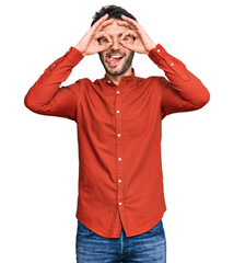 Young hispanic man wearing casual clothes doing ok gesture like binoculars sticking tongue out, eyes looking through fingers. crazy expression.