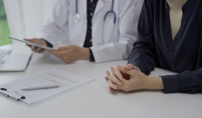 Doctor and a patient in clinic. The female physician is using tablet computer for filling up medication history record form, close up of woman hands. Medicine and science