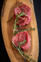 Raw Filet Mignon on a cutting board with rosemary and black pepper.