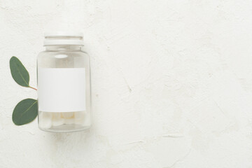 Bottles with pills and green leaves on concrete background, top view