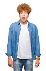 Young handsome man with afro hair wearing denim jacket afraid and shocked with surprise expression, fear and excited face.