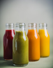 Glass bottles filled with green, yellow, orange and red smoothies. Healthy beverage. Delicious drink