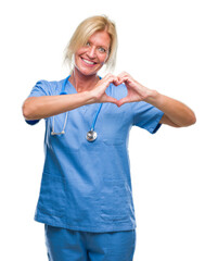 Middle age blonde nurse surgeon doctor woman over isolated background smiling in love showing heart...