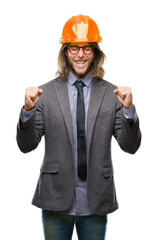 Young handsome architec man with long hair wearing safety helmet over isolated background excited for success with arms raised celebrating victory smiling. Winner concept.