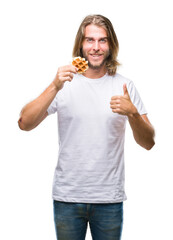 Young handsome man with long hair over isolated background eating waffle happy with big smile doing ok sign, thumb up with fingers, excellent sign