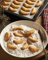 Coating freshly baked Christmas cookies called Kipferl or vanilla crescents in sugar